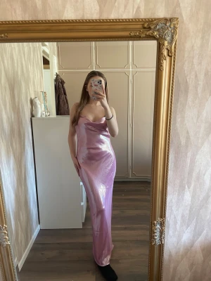 Lång glittrig rosa klänning Gina Tricot - Säljer en lång, glittrig rosa klänning från Gina Tricot. Klänningen har smala justerbara axelband, en snygg vattenfallsdrapering och en figurnära passform. Perfekt för dig som vill sticka ut med en trendig och elegant look. Ny utan prislapp