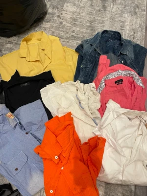 Färgglada skjortor i olika material 8st - Säljer ett blandat paket med skjortor i flera färger: gul, blå, svart, vit, orange, rosa och jeansblå. Skjortorna har klassisk krage och knappar framtill. Några är i bomull, en i denim och andra i lättare material. Perfekt för dig som vill ha variation i garderoben.