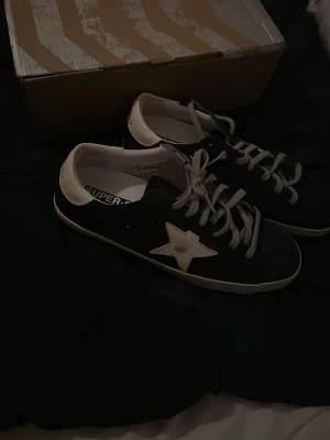 Blåa Golden Goose sneakers - Golden Goose Super-Star sneakers i mörkblått med vit stjärna på sidan och vit häl. Storlek 43. Använts fåtal gånger. Kan lite användning kan man se som att de är lite mer smutsigare. Köptes här på plick. Säljes för 2500kr. Kom med bud gärna. Kontakta mig om du har frågor.