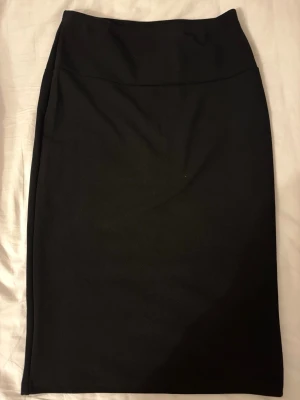 Svart långkjol i enkel stil - En svart långkjol med rak passform och hög midja. Kjolen är stilren och passar perfekt till många olika outfits. Materialet känns mjukt och följsamt, vilket gör den bekväm att bära hela dagen.
