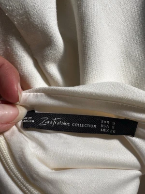 Off white halterneckklänning från Zara - Säljer en stilren vit halterneckklänning från Zara Trafaluc Collection. Klänningen är kort, har en figurnära passform och är tillverkad i ett mjukt tyg som känns bekvämt mot huden. Perfekt för dig som vill ha en enkel men snygg look.