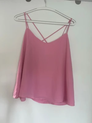 Rosa linnetopp med tunna axelband - Säljer en rosa topp med tunna axelband som korsas i ryggen. Toppen är i storlek M men har en lös passform och en enkel, stilren design med liten spetskant vid urringningen. 