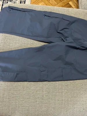 Mörkblå cargobyxor med dragsko - Snygga mörkblå cargobyxor med flera stora fickor på benen och elastisk midja med dragsko. Tillverkade i ett lätt och slitstarkt material som ger en avslappnad och trendig look. Perfekta för dig som gillar streetwear och praktiska detaljer.