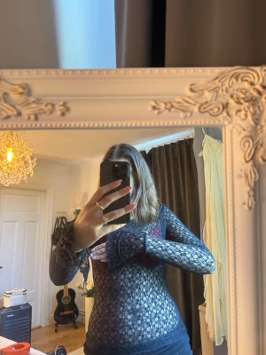 Svart blommig spetsblus långärmad - Säljer en transparent svart långärmad blus i spets med blommigt mönster. Toppen är figurnära och har en snygg v-ringning. Perfekt att styla med ett linne eller en bralette under för en trendig look.
