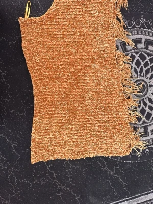 Brun stickad halsduk med fransar - Mysig stickad halsduk i varm brun färg med mjuk, fluffig textur. Halsduken har dekorativa fransar på ena sidan och är rektangulär i formen. Perfekt för att hålla värmen under kyliga dagar och ger en trendig touch till din outfit.