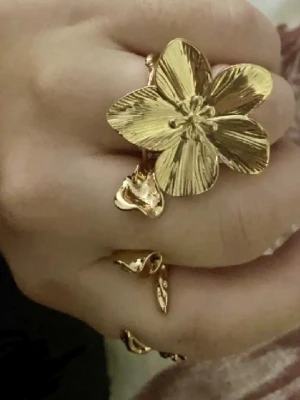 Guldfärgad ring med stor blomma - Unik guldfärgad ring med en stor, detaljerad blomma som blickfång. Ringen har en öppen design och blommans kronblad har fina räfflade detaljer som ger en cool och trendig look. Perfekt för dig som vill sticka ut med dina accessoarer.