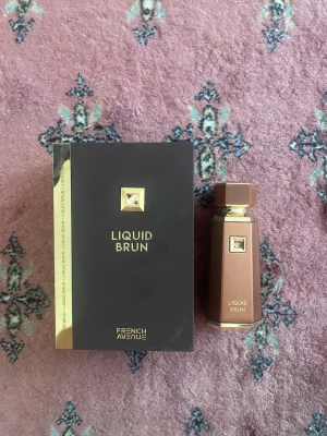 Liquid Brun parfym French Avenue - Liquid Brun parfym från French Avenue med elegant brun och guld färgad flaska och matchande förpackning. Flaskan har en modern, kantig design med gulddetaljer och en fyrkantig kork. Perfekt för dig som gillar lyxiga och stilrena dofter.