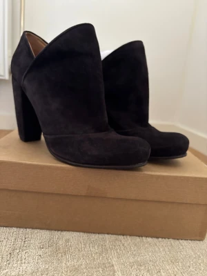 Coclico boots - Snygga svarta stövletter i mocka från Coclico med hög klack och rundad tå. Skorna har en stilren och modern design med högt skaft och bred klack som ger stabilitet. Perfekta för dig som vill ha en trendig och elegant look.