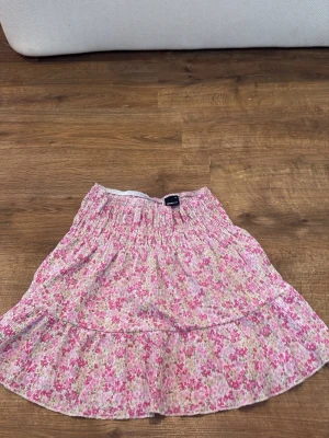 Blommig volangkjol i rosa toner - Söt kjol med volanger och blommigt mönster i rosa, vitt och grönt. Kjolen har resår i midjan och är gjord i ett lätt, luftigt tyg som passar perfekt till sommaren. Den har en avslappnad passform och ger en romantisk vibe. Den är från Gina men säljs inte längre då jag köpte den förra året men andvände ej den tror original priset är runt 249kr 