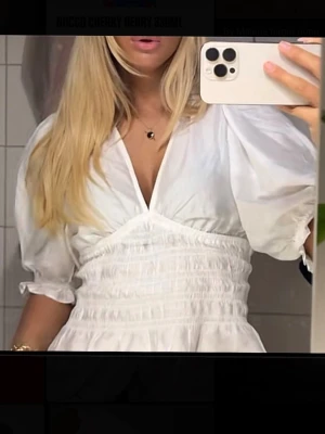 Vit blus med puffärm och v-ringning - Snygg vit blus med djup v-ringning och puffiga trekvartsärmar. Blusen har smockad midja som ger en feminin siluett och volangkant nedtill. Tillverkad i ett lätt tyg som känns luftigt och fräscht. Perfekt att styla med jeans eller kjol.