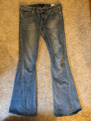 Bootcut jeans från True Religion - blå bootcut jeans från True Religion med grön/gul stiching. Hade jål mellan benen men har sytt ihop de igen.