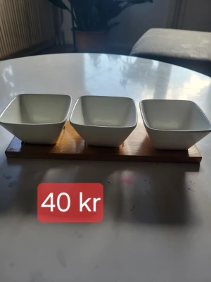 Vita skålar på träbricka Collection - Tre fyrkantiga vita skålar i porslin från Collection, placerade på en rektangulär träbricka. Perfekt för snacks, dippar eller tillbehör. Enkel och stilren design som passar i de flesta kök.