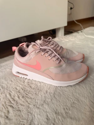 Nike rosa sneakers med meshdetaljer - Säljer ett par snygga Nike sneakers i ljusrosa med korallfärgade detaljer och vit sula. Skorna har meshpartier för extra ventilation och klassisk Nike-logga på sidan. Perfekta för dig som gillar sportig stil och vill ha bekväma skor till vardags.