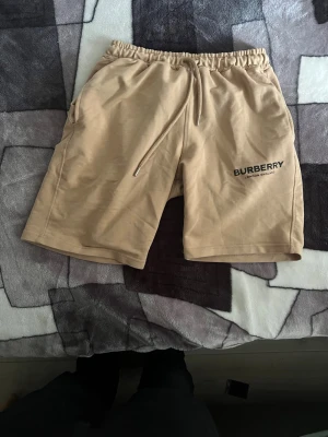 Beige shorts med snörning Burberry - Snygga beige shorts från Burberry med elastisk midja och snörning framtill. Shortsen har en avslappnad passform, sidofickor och diskret Burberry-logga på vänster ben. Tillverkade i mjuk bomull, perfekta för varma dagar.