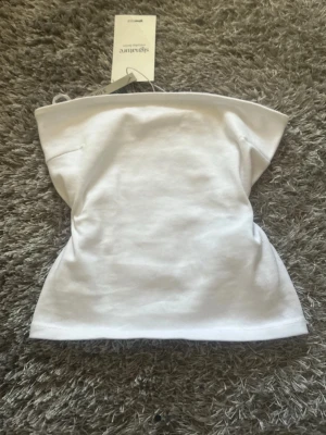 Vit axelbandslös tubtopp - Snygg vit tubtopp i mjukt bomullsmaterial. Axelbandslös bandeau-modell som sitter tight och är perfekt till sommaren. Enkel och stilren design som passar till allt.