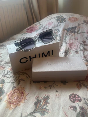 Chimi 04 - Snygga solglasögon från CHIMI i transparent grå plast med fyrkantiga bågar och mörka glas. Kommer med originaletui och box. Perfekta för dig som vill ha en stilren och modern look.