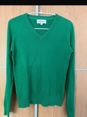 Grön stickad tröja från Berkeley - Snygg grön stickad tröja från Berkeley med v-ringning och långa ärmar. Tröjan har ribbade muddar vid ärmslut och nederkant, vilket ger en klassisk och clean look. Perfekt att matcha med jeans eller kjol för en chill stil.