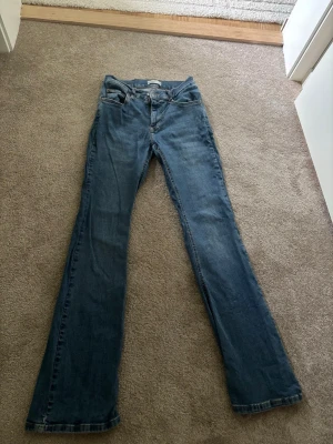 Blå bootcut jeans - Säljer ett par klassiska blå bootcut jeans i denim med normal midja. Jeansen har en lätt tvättad look och raka ben som går ut något nedtill. Perfekta till sneakers eller boots för en avslappnad stil.