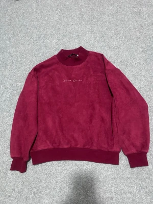 Vinröd sweatshirt med hög krage - Säljer en vinröd sweatshirt med hög ribbad krage och muddar. Tröjan har broderad text 'Blend Child' på bröstet och är gjord i ett mjukt, sammetsliknande material. Perfekt för dig som gillar en avslappnad men ändå stilren look.
