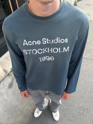 Acne studios longsleeve - Säljer en blå långärmad t-shirt från Acne Studios med tryck 'Acne Studios STOCKHOLM 1996' på bröstet. Skön passform och klassisk rund hals. Perfekt för dig som gillar stilrena och trendiga plagg.