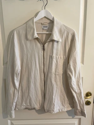 Beige overshirt från Weekday - Stilren beige overshirt från Weekday med dragkedja framtill och en bröstficka. Overshirten har klassisk krage och är tillverkad i ett mjukt, strukturerat tyg som känns skönt mot huden. Perfekt att slänga över en t-shirt för en avslappnad look.