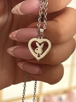 Halsband med hjärta och kaninmotiv - Playboy halsband i kirurgisktstål. Kedjan är tunn och stilren, perfekt för att ge din outfit en lekfull touch. OBSERVERA jag kommer vara bortrest mellan 14:e juli fram till 5:e augusti. Om köpet läggs före jag reser så skickar jag inom 1-2 dagar och annars skickas det efter hemresan. 