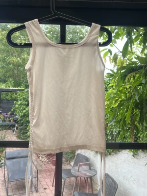 Vit ribbad linnetopp med snörning - Säljer en ljusbeige ribbad linnetopp med snörning i sidorna. Toppen är ärmlös och har en rund halsringning. Perfekt för sommardagar och enkel att styla med olika outfits.