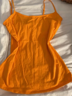 Orange nattlinne med smala axelband - Snyggt orange nattlinne i mjukt och lätt material med smala axelband och enkel, rak passform. Perfekt för varma nätter eller mysiga hemmakvällar. Färgen är klar och ger en fräsch känsla.