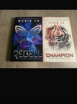 Legend-serien: Rebell & Champion - Två böcker av Marie Lu ur Legend-serien: 'Rebell' med ett blått och lila omslag med fjärilsmotiv, och 'Champion' med vitt omslag och en svart/röd ros. Båda är inbundna och har snygga, moderna omslag. Perfekt för dig som gillar dystopisk ungdomslitteratur. Inbundna!!