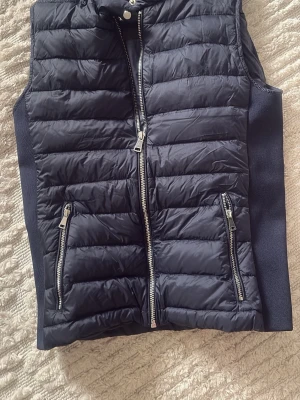 Mörkblå dunväst från Zara Woman - Snygg mörkblå dunväst från Zara Woman med quiltad design och två dragkedjeförsedda fickor framtill. Västen har hög krage och blanka silverfärgade dragkedjor. Perfekt för lager på lager och ger en sportig look.