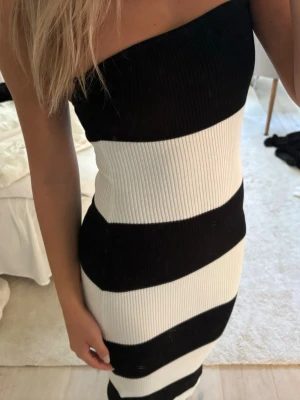Svartvit ribbad one shoulder klänning - Säljer en snygg svartvit klänning med breda diagonala ränder. Klänningen är ribbad och har en one shoulder-design som ger en trendig look. Materialet är stretchigt och figurnära, perfekt för dig som vill sticka ut.