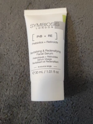 Symbiosis London ansiktsserum 30ml - Revitalising & Redensifying Facial Serum med prebiotika och retinoider. Vit tub med svart text, 30 ml. Perfekt för dig som vill boosta huden med extra näring och lyster.
