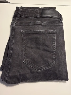 Svarta jeans från Dressmann - Säljer ett par svarta jeans från Dressmann med klassisk femficksdesign och dragkedjegylf. Jeansen har raka ben och är tillverkade i ett mjukt denimtyg med lite stretch för extra komfort. Perfekta till en avslappnad stil.