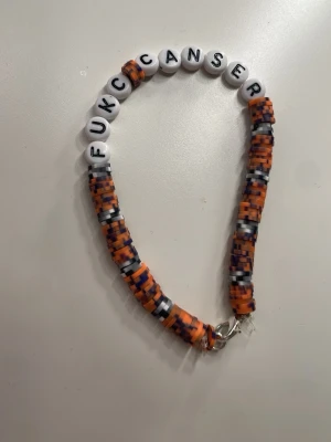 Pärlarmband med text FU*K CANSER - Färgglatt armband med vita bokstavspärlor som stavar 'FUCK CANSER'. Resten av armbandet består av små pärlor i orange, svart, vitt och blått. Armbandet har ett metallspänne och är handgjort i plastpärlor. Skickar pengarna till cancer fonden, ❤️‍🩹