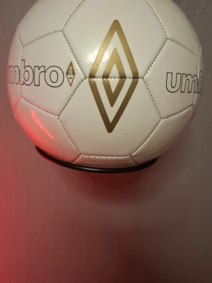 Vit fotboll från Umbro storlek 4 - Säljer en klassisk vit fotboll från Umbro i storlek 4. Bollen har guldiga detaljer och Umbros logga tryckt på flera sidor. Perfekt för dig som vill lira på planen eller träna skott med stil.