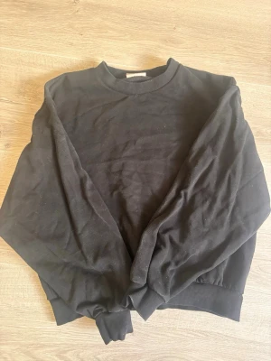 Svart sweatshirt från Gina Tricot - En klassisk svart sweatshirt från Gina Tricot med rund halsringning och ribbade muddar vid ärmslut och nederkant. Perfekt basic-plagg att ha i garderoben och lätt att matcha med allt.