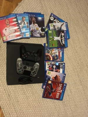 PlayStation 4 med spel och två kontroller - Säljer en svart PlayStation 4 med två handkontroller, en i svart och en i genomskinlig design. Medföljer flera populära spel som FIFA, Spider-Man och Lego Avengers. Perfekt för gamingkvällar med vänner eller familj. Finns från FIFA 17-25.