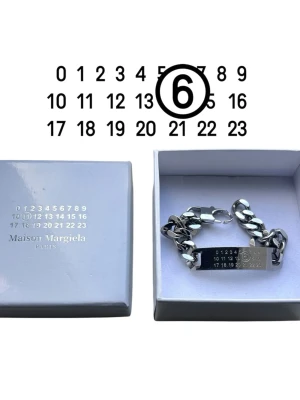 Maison Margiela silverarmband - Snyggt silverfärgat armband från Maison Margiela med deras ikoniska siffror och logga ingraverat på en platta. Kraftig kedja i metall ger en cool och modern look. Kommer i original ask. MM6 by Margiela, bra skick. 