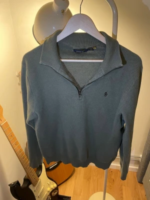 Grå halvzip tröja från Polo Ralph Lauren - Snygg grå stickad tröja från Polo Ralph Lauren med halv dragkedja och klassisk krage. Tröjan har diskret logga broderad på bröstet och ribbade muddar vid ärmslut och nederkant. Perfekt till jeans eller chinos.