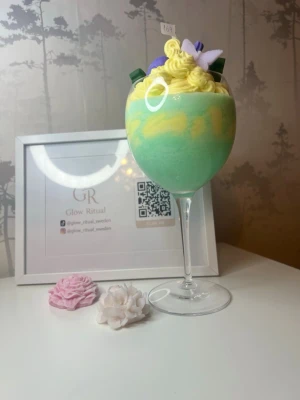 Glow Ritual dekorljus i glas - Unikt doftljus i glas från Glow Ritual, utformat som en dessert, toppat med dekorativa blommor i lila och vitt samt grönbladiga detaljer. Perfekt som inredningsdetalj för dig som gillar färgglada och kreativa ljus.