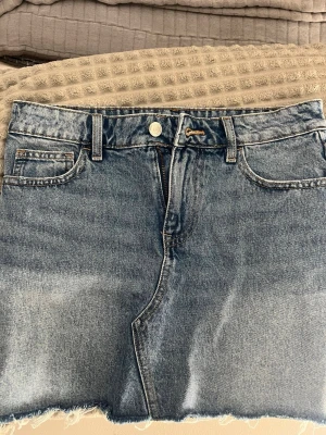 Blå jeanskjol med broderade bakfickor - Säljer en snygg blå jeanskjol från Gina Tricot med broderade detaljer på bakfickorna. Säljer den för den har inte kommit till användning