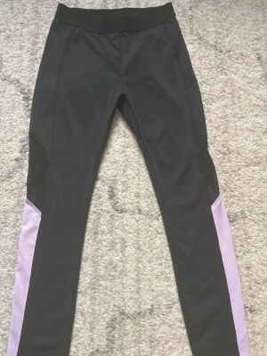 Svarta träningsleggings från SOC - Snygga svarta träningsleggings från SOC med lila paneler längs benen. Tillverkade i ett tekniskt material med TCS Airflow som håller dig torr och bekväm under träningen. Perfekta för gym, löpning eller annan sport.