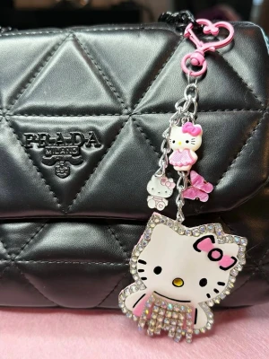 Hello Kitty nyckelring med strass - Söt Hello Kitty nyckelring med flera hängen, bland annat en stor Hello Kitty med strassdetaljer och rosa rosett. Kedjan har även små figurer och rosa detaljer. Perfekt som accessoar till väskan eller nycklarna.