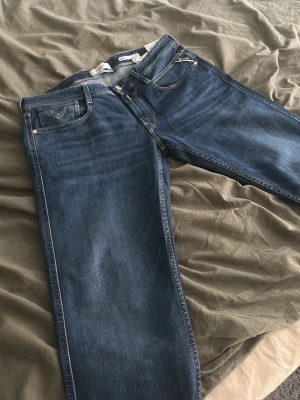Jeans från replay  - Klassiska blå jeans från replay. Jeansen har en snygg tvätt med lätt slitning och detaljer i silverfärg vid fickorna. Perfekta för en avslappnad och stilren look.