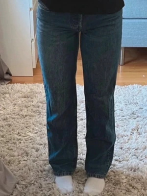 Blå raka jeans med låg/mid midja - Säljer ett par klassiska blå jeans med rak passform och hög midja. Jeansen har en tidlös tvätt och är tillverkade i ett robust denimtyg. Perfekta för en avslappnad och trendig look.