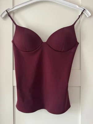 Vinröd linnetopp - Säljer en vinröd linnetopp med bygel och tunna axelband. Toppen har en figurnära passform och slät yta, Materialet känns mjukt och följsamt mot huden. ALDRIG ANVÄNT, köp gärna via insta box❤️