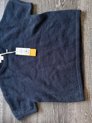 Mörkblå tshirt kort ärm - Mysig mörkblå topp i mjuk ull med rund hals och korta ärmar. Enkel och stilren design som passar perfekt till både jeans och kjol. Materialet känns lyxigt och håller dig varm under kyligare dagar.