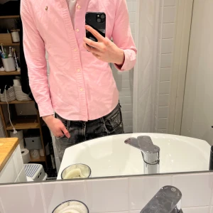 Rosa skjorta från Ralph Lauren - Säljer en snygg rosa skjorta från Ralph Lauren med klassisk krage och broderad logga på bröstet. Skjortan har långa ärmar och knäppning framtill. Perfekt för dig som vill ha en stilren och trendig look.