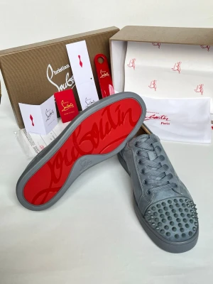 Grå Christian Louboutin sneakers med nitar - Snygga grå sneakers från Christian Louboutin i mocka med ikonisk röd sula och coola nitar på tån. Skorna har klassisk låg modell, matchande grå snörning och exklusiv känsla. Perfekta för dig som vill sticka ut med stil och attityd.