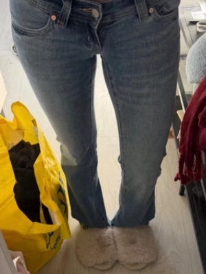 Blå bootcut jeans med läderpatch - Säljer ett par klassiska blå bootcut jeans med fem fickor och en liten brun läderpatch på bakfickan. Jeansen har normalhög midja och är tillverkade i ett mjukt denimtyg. Perfekta för en avslappnad och trendig look. Jeansen är aldrig använda endast testade men ingen lapp kvar. Storlek 24 tall. Passar mig perfekt i längden och är 170cm
